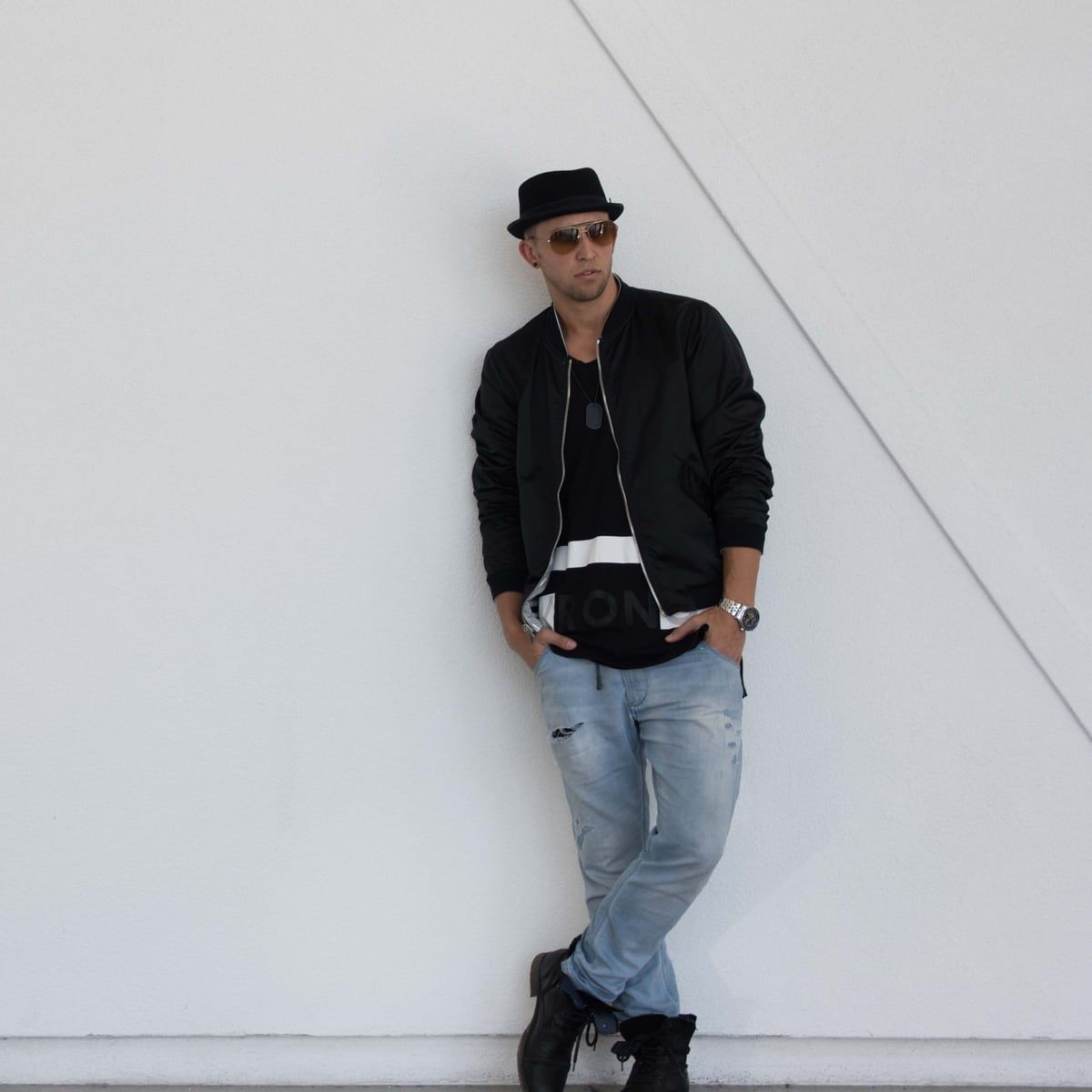 Matt in a black hat leaning on a white gallery wall